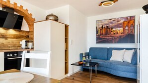 A compact living space with a kitchenette, a dining area, a sofa, and a cityscape painting.