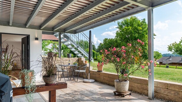 An outdoor patio with a covered seating area, potted plants, and a staircase leading to an upper level.