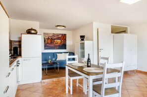 Uma cozinha compacta com armários brancos, uma mesa de jantar com cadeiras, um sofá e um quadro na parede.
