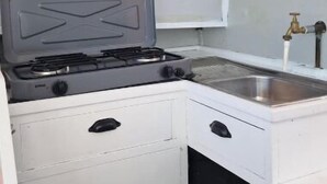 Una cocina compacta con estufa a gas, un lavamanos y un mueble pequeño.