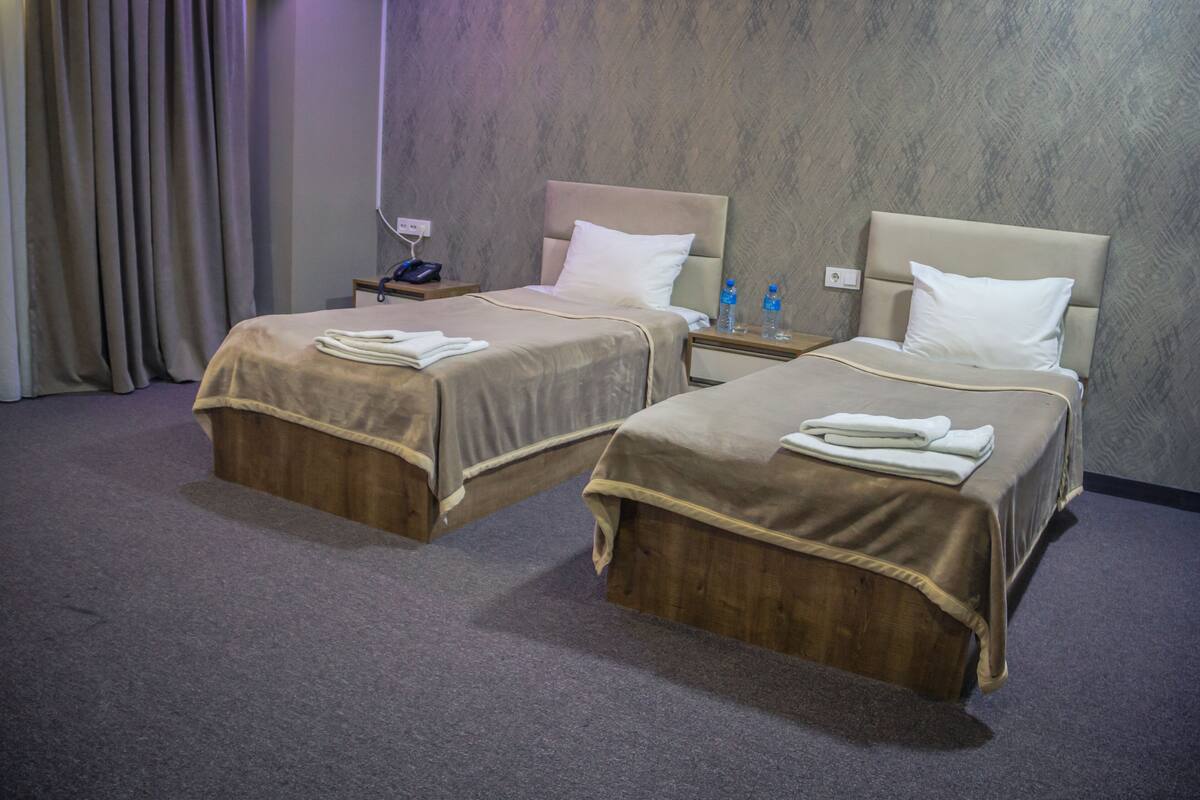 A hotel room with two beds, each with a headboard, a nightstand, and a lamp.