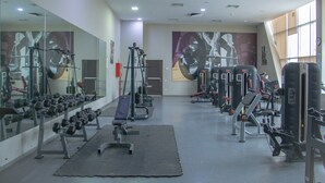 Un gimnasio con equipos de ejercicio variados, espejos y un amplio ventanal.