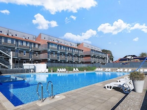 A swimming pool with lounge chairs and a building with multiple balconies in the background.