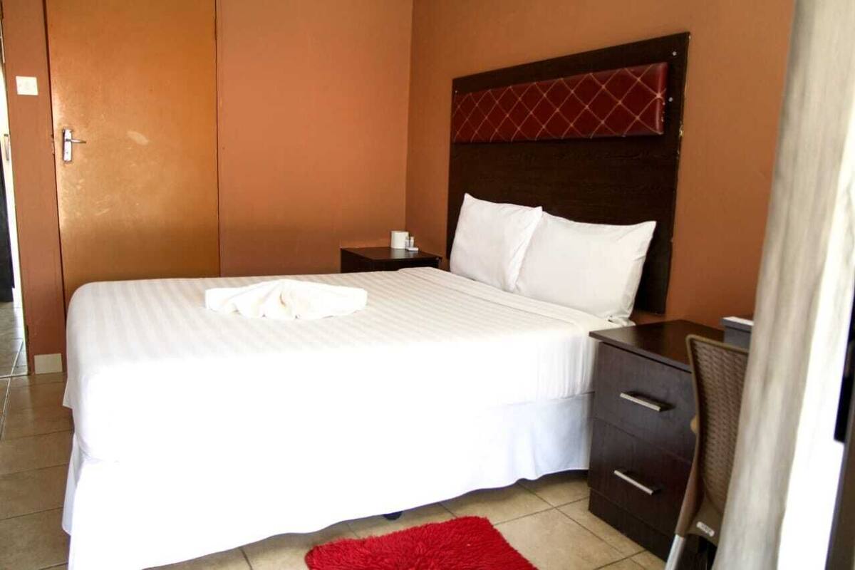 A hotel room with a large bed, a wooden headboard, a nightstand, and a desk.