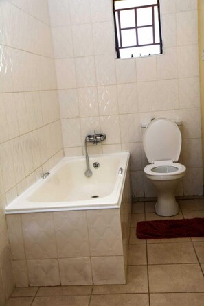A bathroom with a bathtub, toilet, and a small window. - Dream Catcher Hotel (Gaborone)