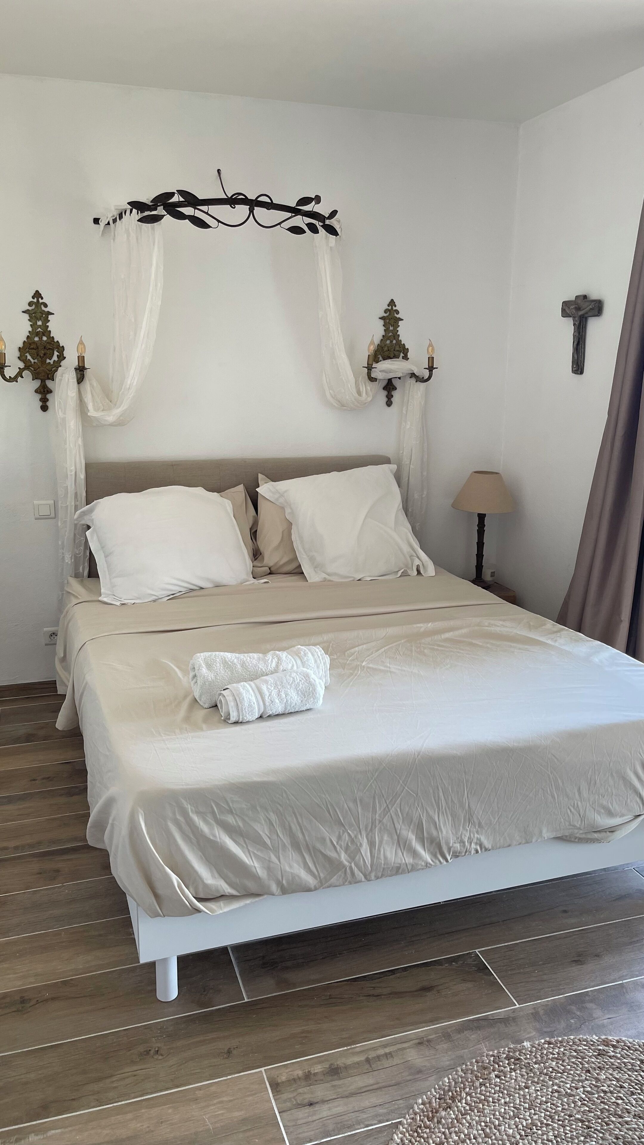 A neatly made bed with white linens, a white headboard, and a decorative wall sconce.