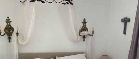 A neatly made bed with white linens, a white headboard, and a decorative wall sconce.