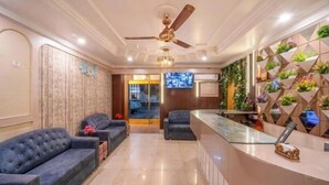 Een hotel lobby met een receptiebalie, twee banken, een plafondventilator en een wand met een plantenarrangement in geometrische vorm.