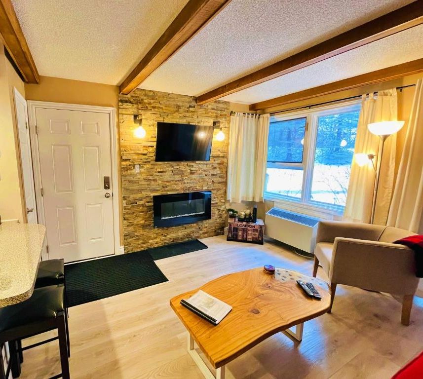 Una sala de estar acogedora con pared de piedra, televisor de pantalla plana, mesa de centro de madera y un sillón cómodo.