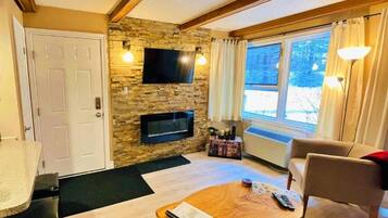 Una sala de estar acogedora con pared de piedra, televisor de pantalla plana, mesa de centro de madera y un sillón cómodo.