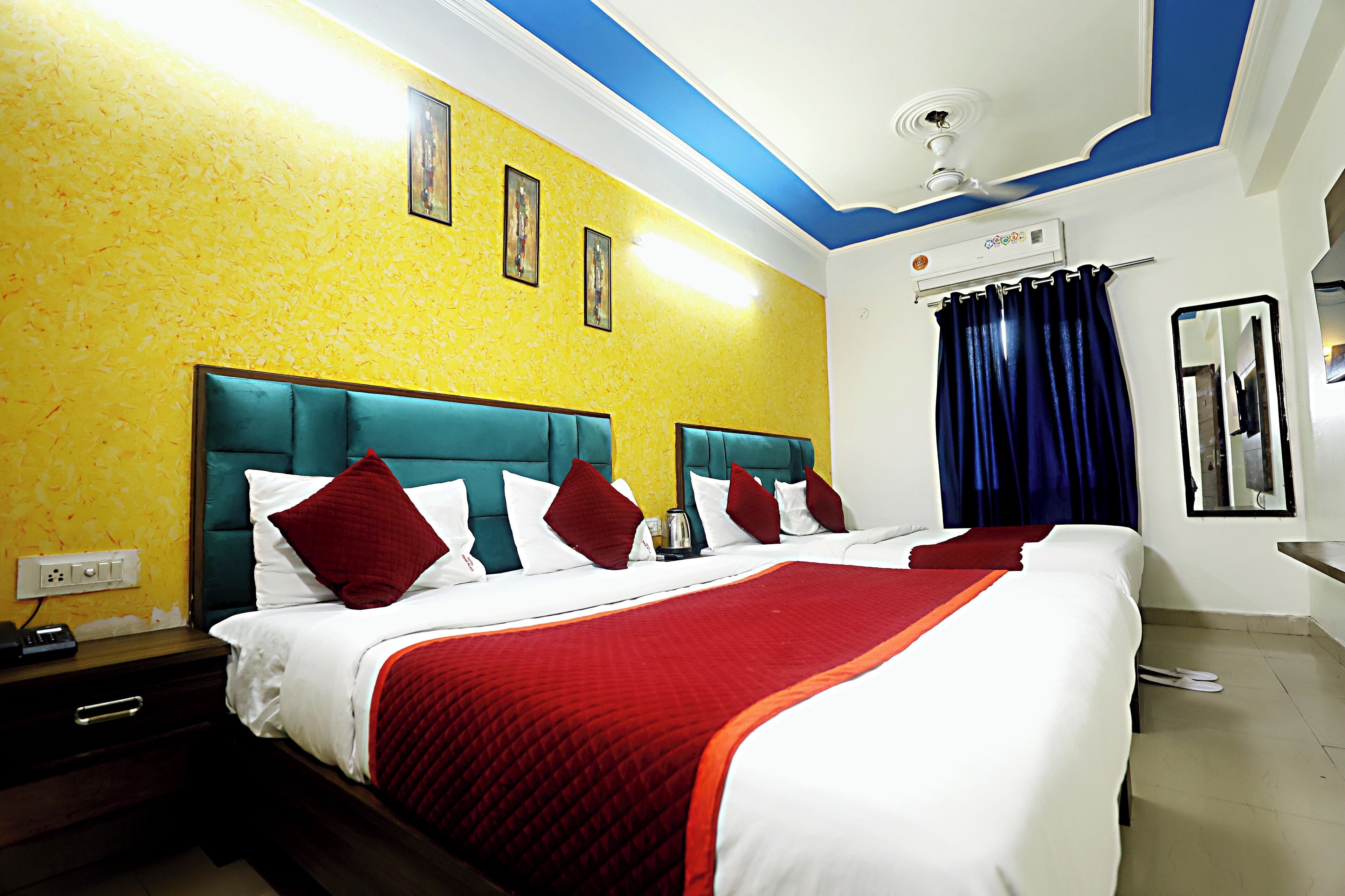 A hotel room with a large bed, two bedside tables, a ceiling fan, an air conditioning unit, and a mirror on the wall.