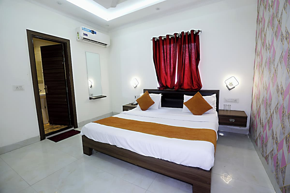 A bedroom with a large bed, a wooden headboard, a red curtain, bedside lamps, and a wall-mounted air conditioner.
