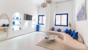 Un salon moderne avec un canapé beige, des coussins bleus, une table basse en verre et un grand miroir.