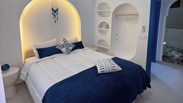 Une chambre moderne avec un lit, des tables de chevet, une étagère fixée au mur et une porte.