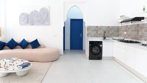 Un salon moderne avec un canapé, une table basse et une porte bleue donnant sur une cuisine équipée d’un lave-linge.