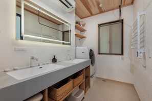 Une salle de bain moderne avec deux lavabos, un miroir, un lave-linge et des étagères en bois.