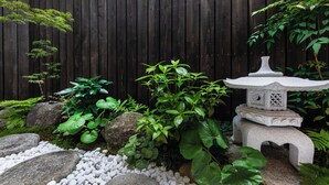 Un giardino con una lanterna in pietra, diverse piante e una recinzione in legno.