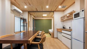 Una cucina moderna con soffitto in legno, una zona pranzo con un tavolo lungo e sedie, e un piccolo letto sullo sfondo.