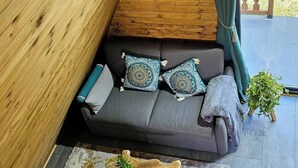 Een gezellig cabin interieur met een houten plafond, een grijze bank met gekleurde kussens, een houten salontafel met een plant, en een bordje met de tekst 'HOME SWEET HOME'.