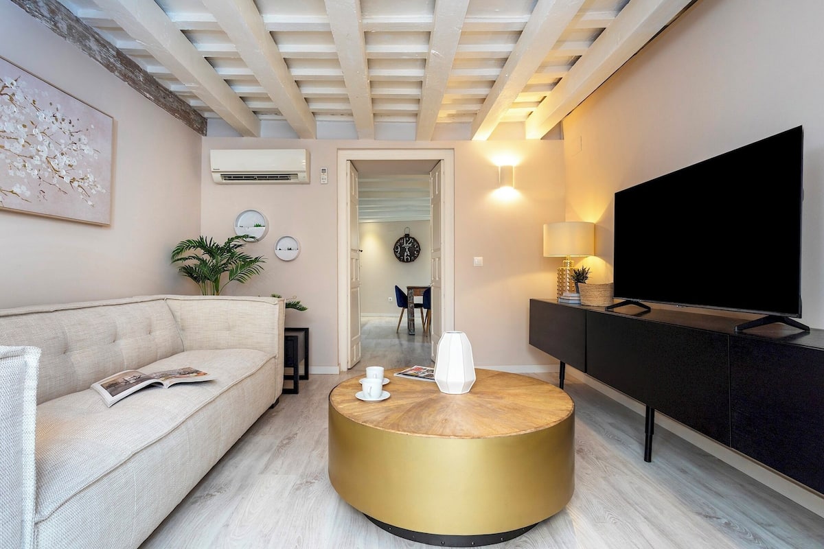 Un salon moderne avec un canapé, une table basse ronde, un téléviseur et, au fond, un coin repas.