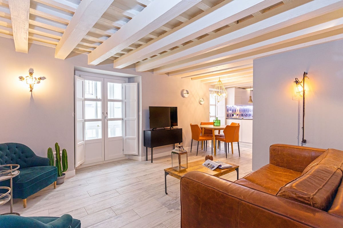 Un salon moderne avec un canapé, un téléviseur, un coin repas et une cuisine en arrière-plan.