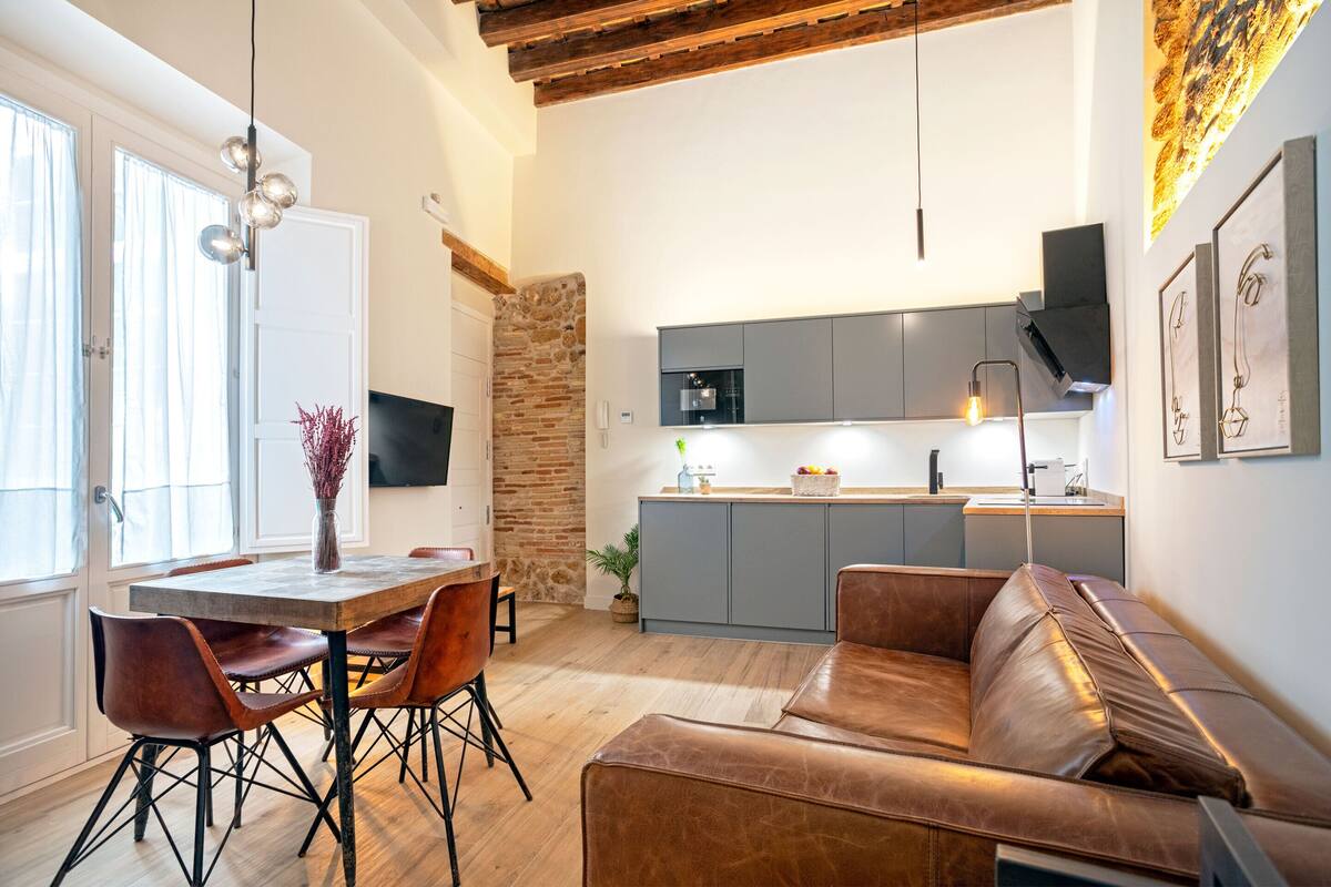 Une cuisine moderne avec des meubles gris, un four encastré et un coin repas comprenant une table en bois et des chaises en cuir.
