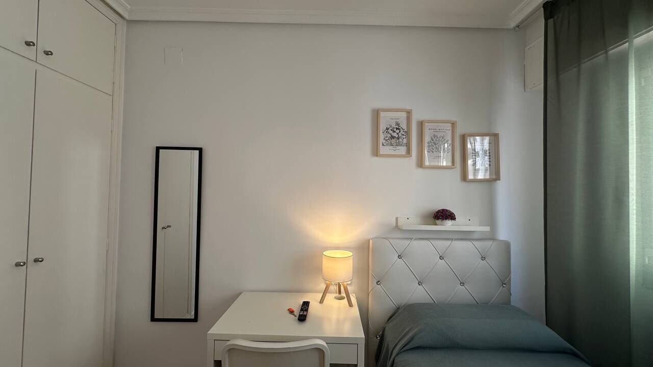 Un dormitorio con cama, mesita de noche, lámpara, espejo y cuadros en la pared.
