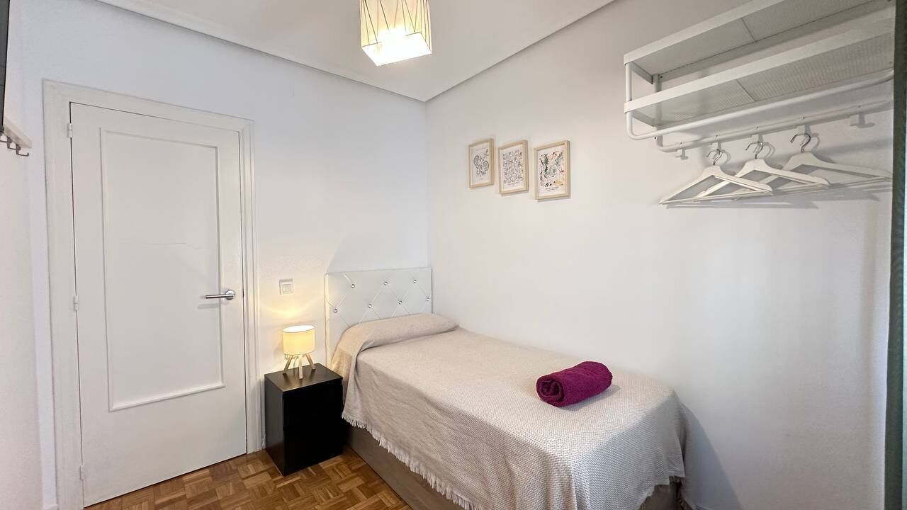 Un dormitorio con cama, mesita de noche, una puerta y perchero en la pared.