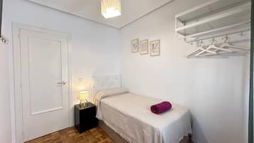 Un dormitorio con cama, mesita de noche, una puerta y perchero en la pared.