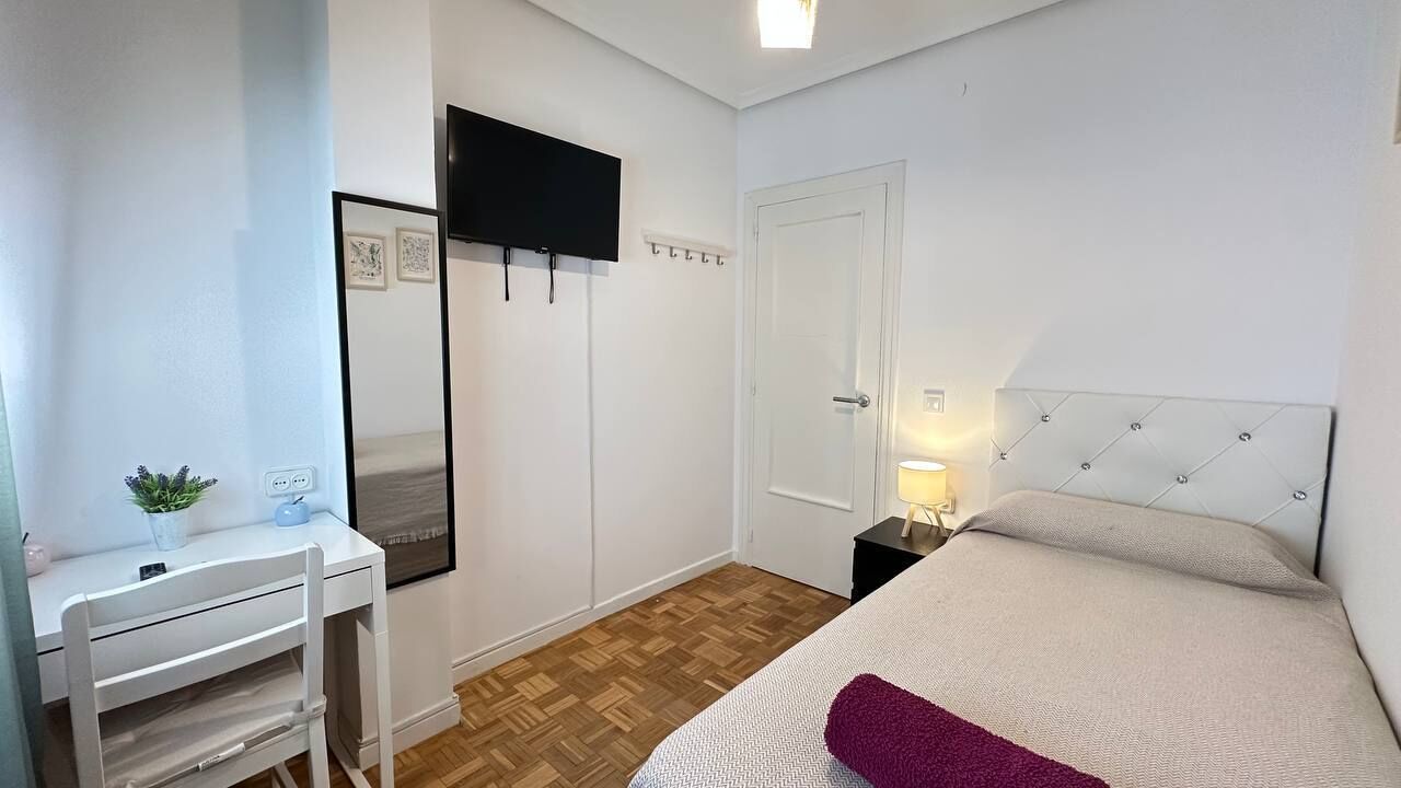 A bedroom with a bed, bedside table, lamp, and a TV mounted on the wall.