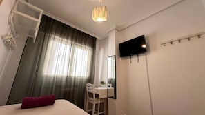 A hotel room with a bed, a desk, a chair, a TV, and a window with curtains. - Habitaciones en Ferrocarril (Madrid)
