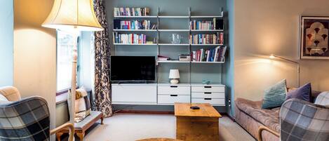 A living room with a TV, bookshelves, a coffee table, and plaid furniture.