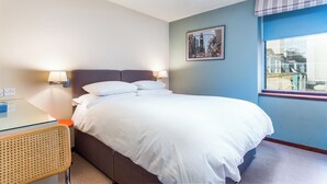 Ein Hotelzimmer mit Bett, Nachttischen, einer Lampe, einem Rattan-Sessel, einem Fenster mit Aussicht und einem Wandbild.
