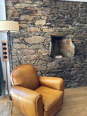 Una habitación con pared de piedra, un sillón de cuero, una lámpara y suelo de madera.