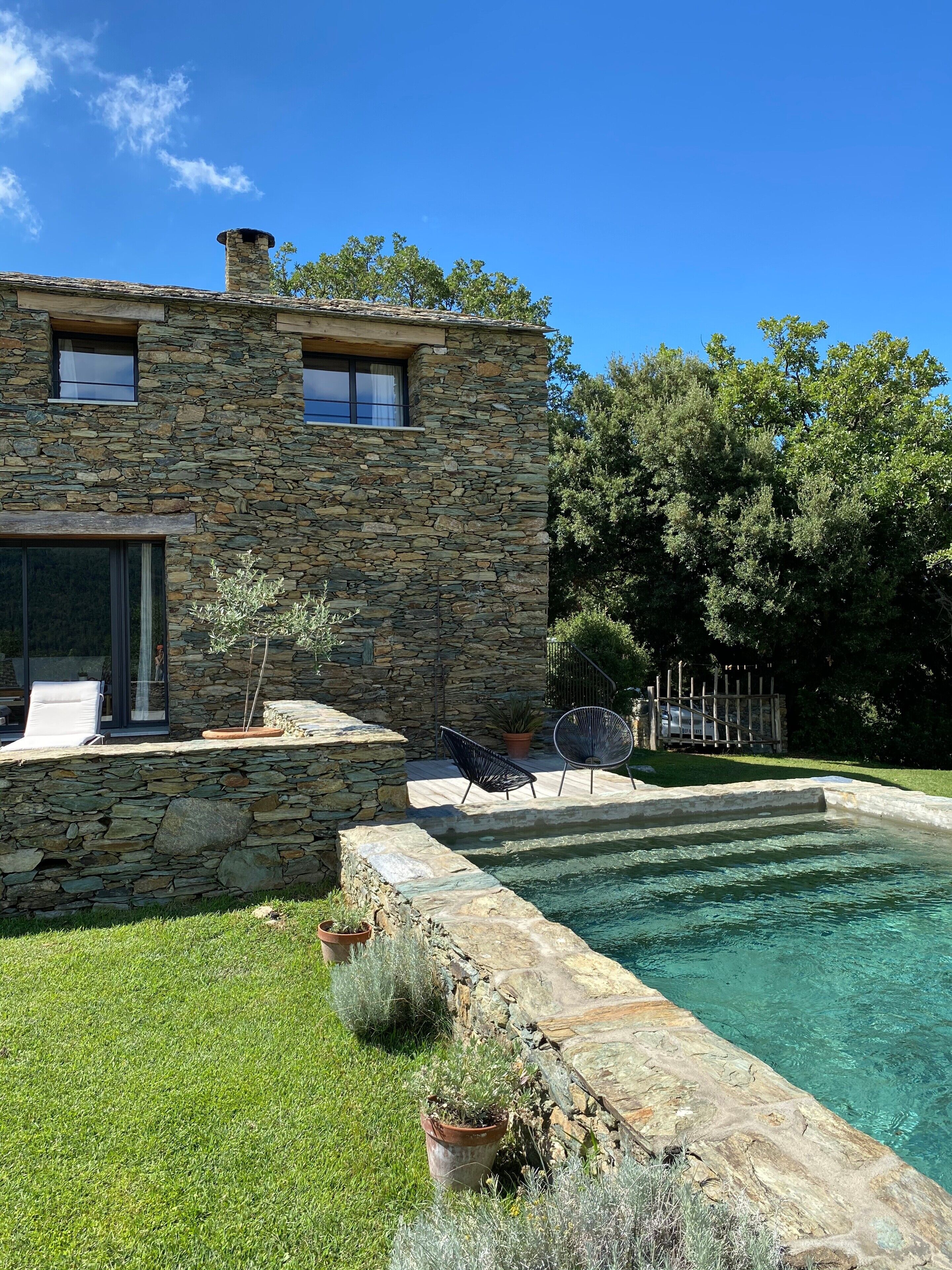 A stone house with a swimming pool, outdoor seating, and a fenced garden.