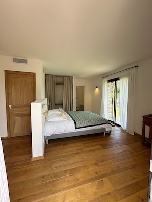 Un dormitorio con piso de madera, una cama con colcha verde, una puerta de madera y una ventana con cortinas.