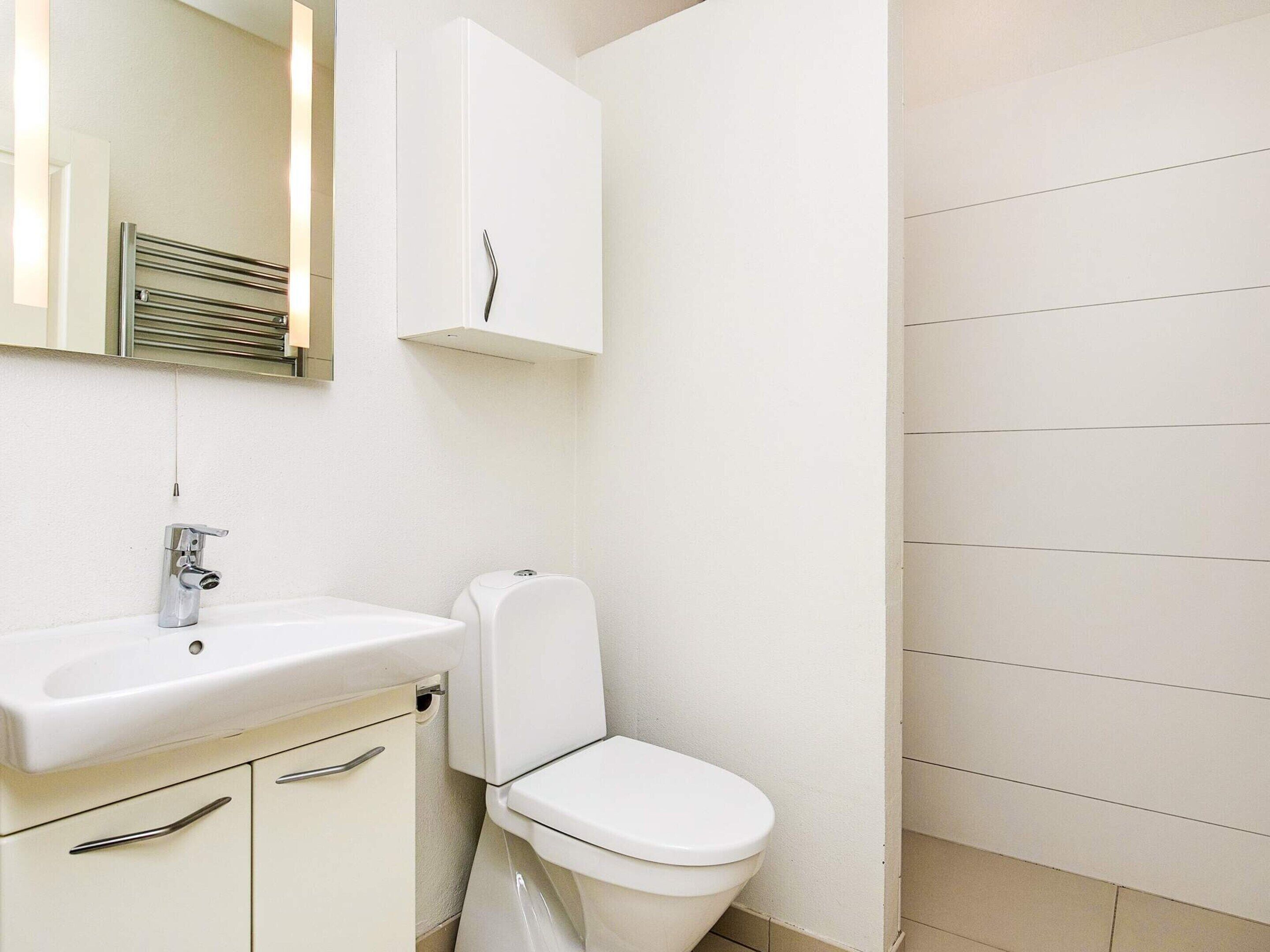Een badkamer met een wit wastafel, een toilet en een kastje met een spiegel erboven.