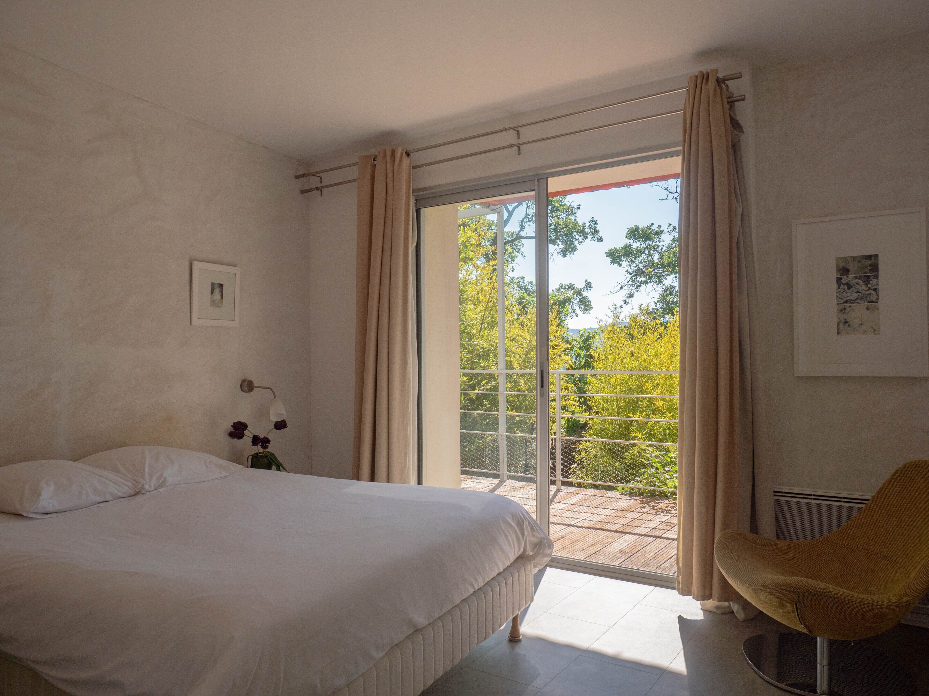 Camera da letto con un letto, una sedia, un comodino, una lampada e vista all'esterno tramite una porta scorrevole in vetro.