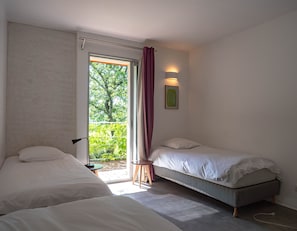 Ein Schlafzimmer mit zwei Betten, einem Fenster mit Vorhängen, einem kleinen Tisch und einer Wandleuchte.