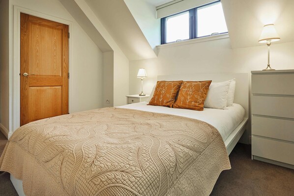 A bedroom with a large bed, a nightstand, a dresser, and a window with a view.