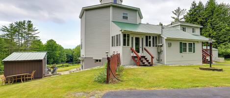 A two-story house with a green roof, a covered porch, and a small shed.