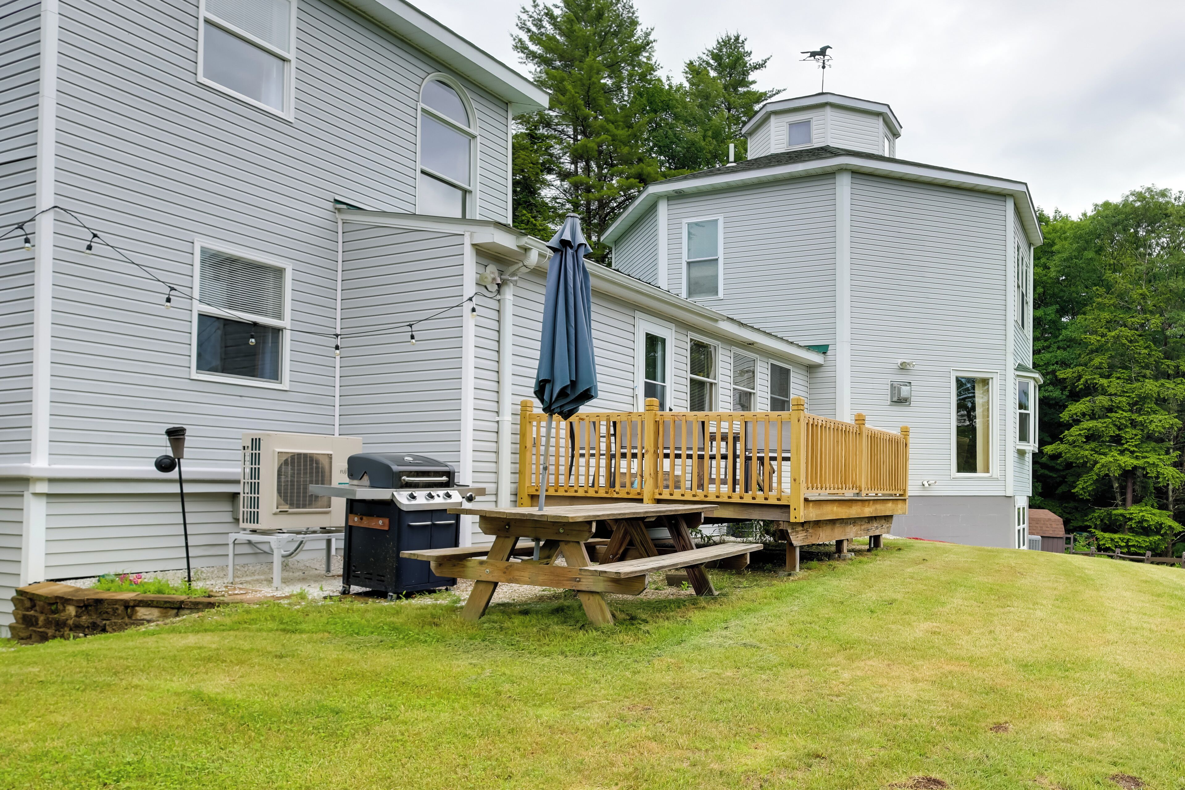 Une maison à deux étages dotée d’une terrasse en bois, d’un barbecue et d’une table de pique-nique couverte.