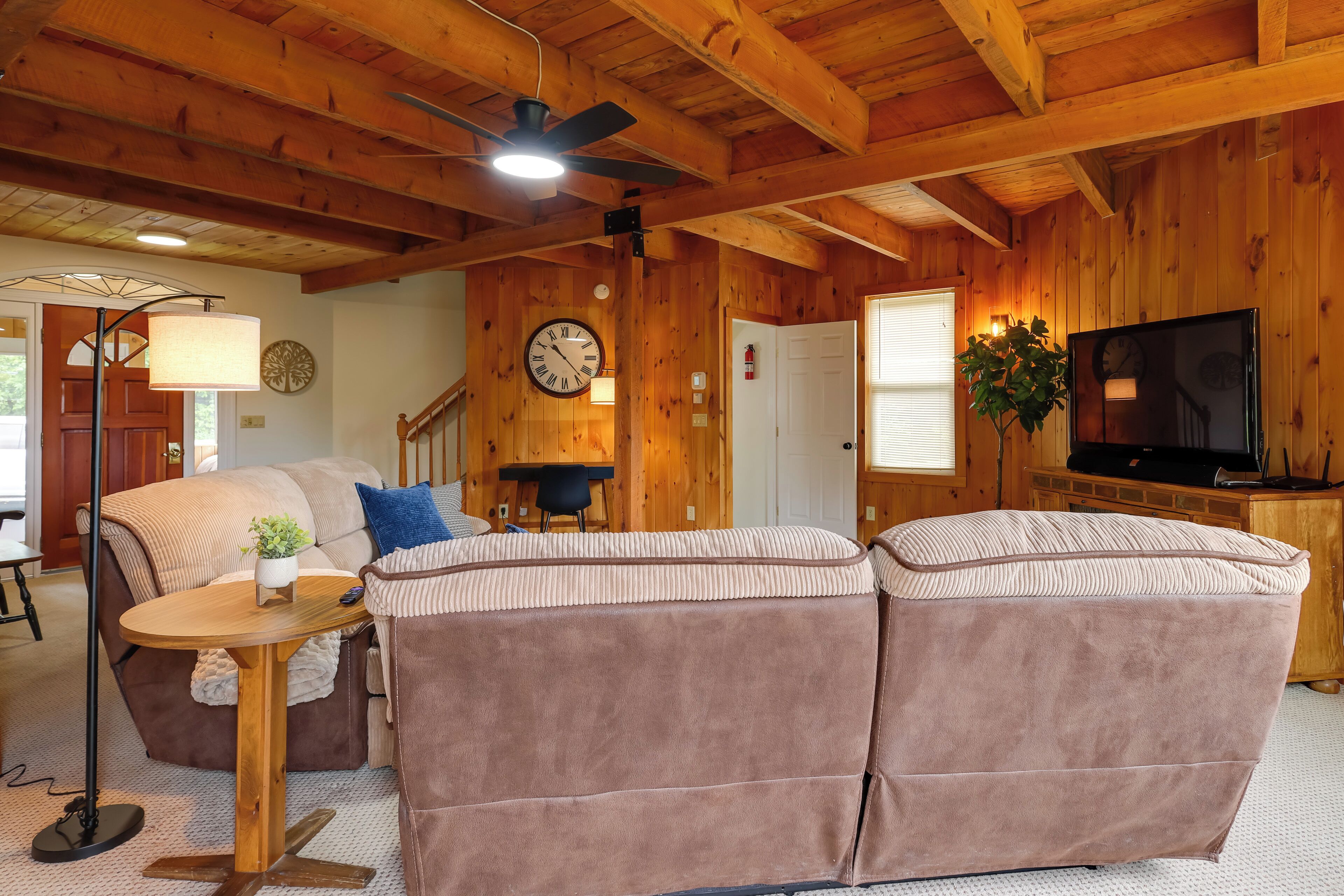 A cozy room with a wooden ceiling, a sofa, a small table, a clock, and a television.