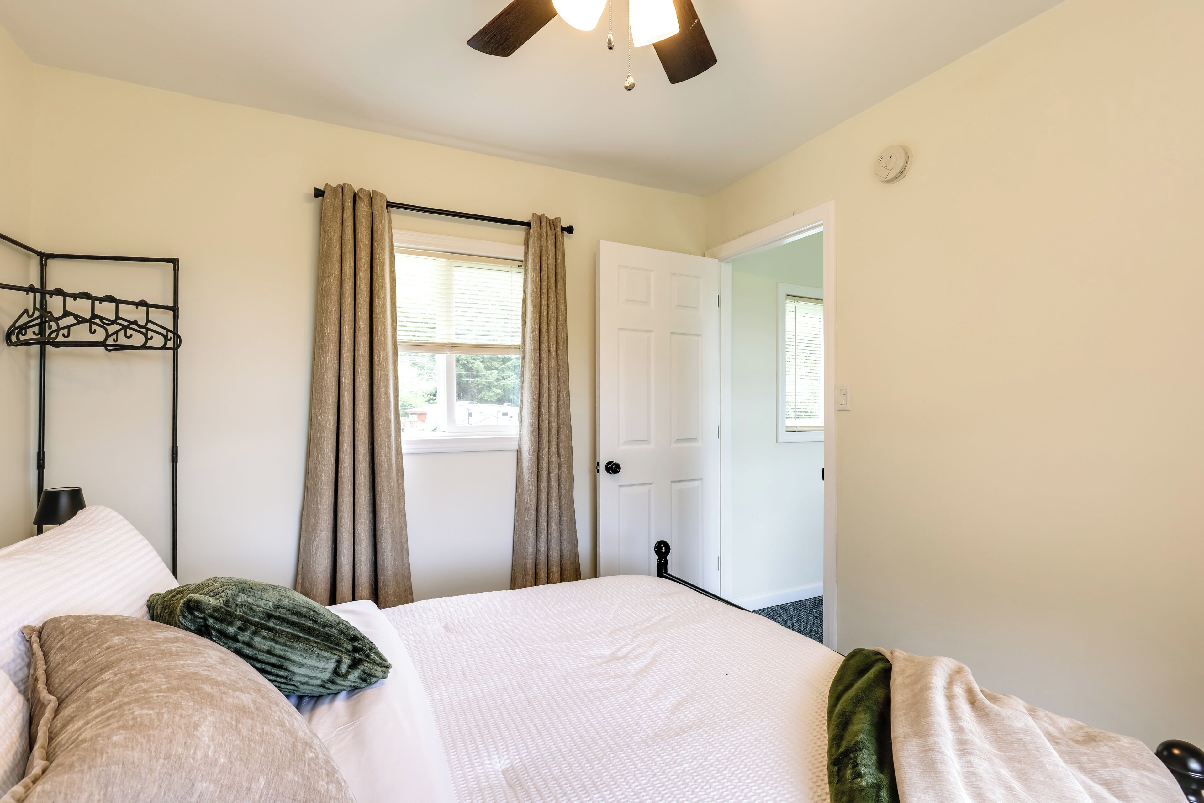 A bedroom with a bed, a coat rack, a door, and a window with curtains.