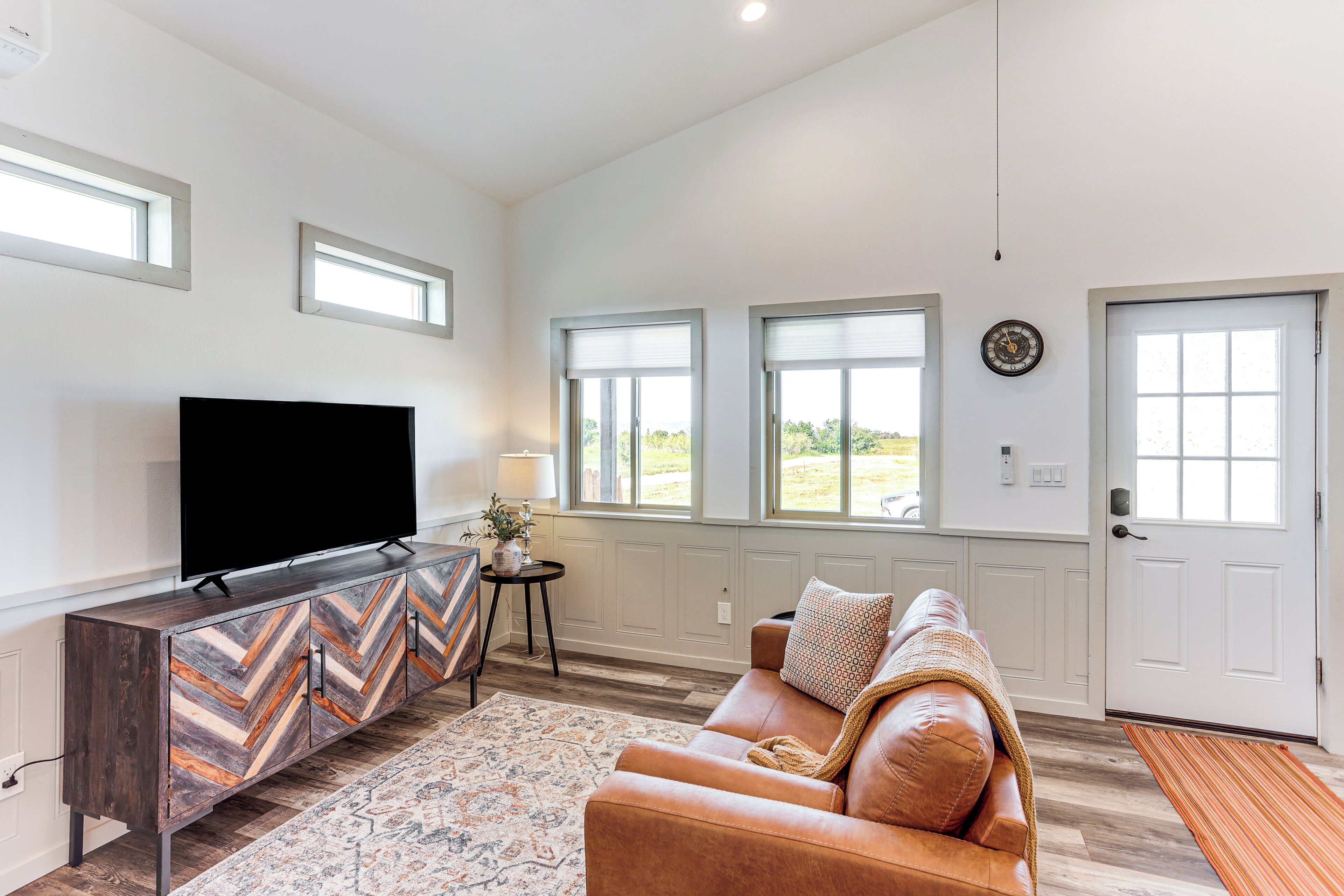 A living room with a flat-screen TV, a chevron-patterned cabinet, a brown leather sofa, and a patterned rug.
