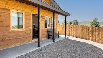 A wooden cabin with a covered porch, gravel ground, and a wooden fence.