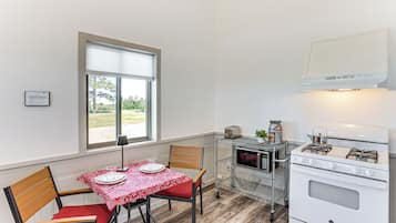 A compact kitchen with a dining table set for two, a microwave, a gas stove, and a small window providing natural light.