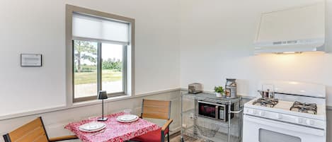 A compact kitchen with a dining table set for two, a microwave, a gas stove, and a small window providing natural light.