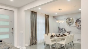 A dining area with a table set for four, white chairs, and a decorative wall clock. - 3 Mi to Tobyhanna State Park: Hot Tub Haven! (Tobyhanna)