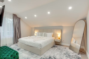 Une chambre moderne avec un grand lit, des lampes de chevet, un miroir et un pouf vert.